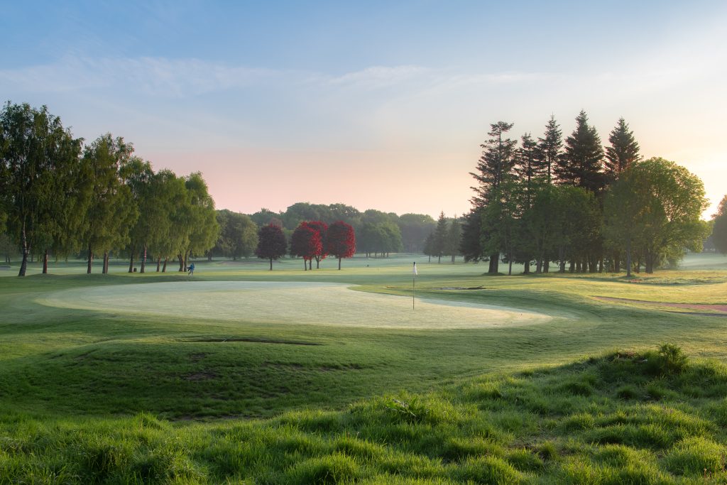well trimmed golf hole in the early morning with mist of the fairway