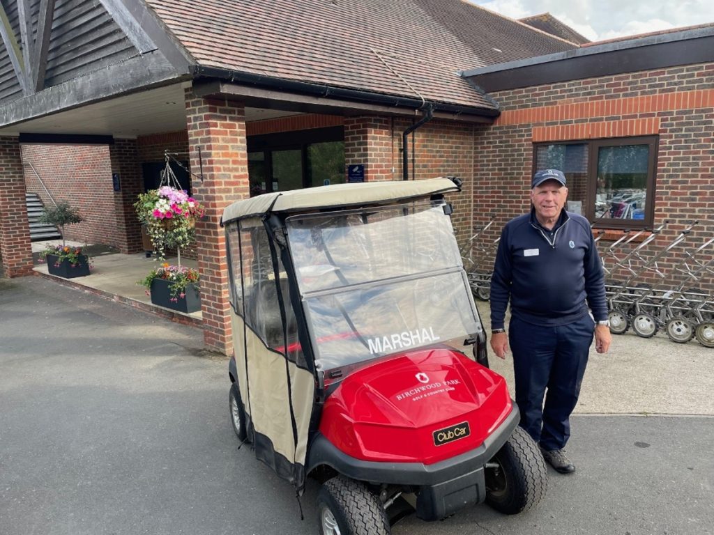 golf marshal standing next to buggy at a golf company