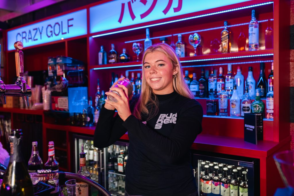 bar tender at crazy golf venue smiling whilst making a cocktail